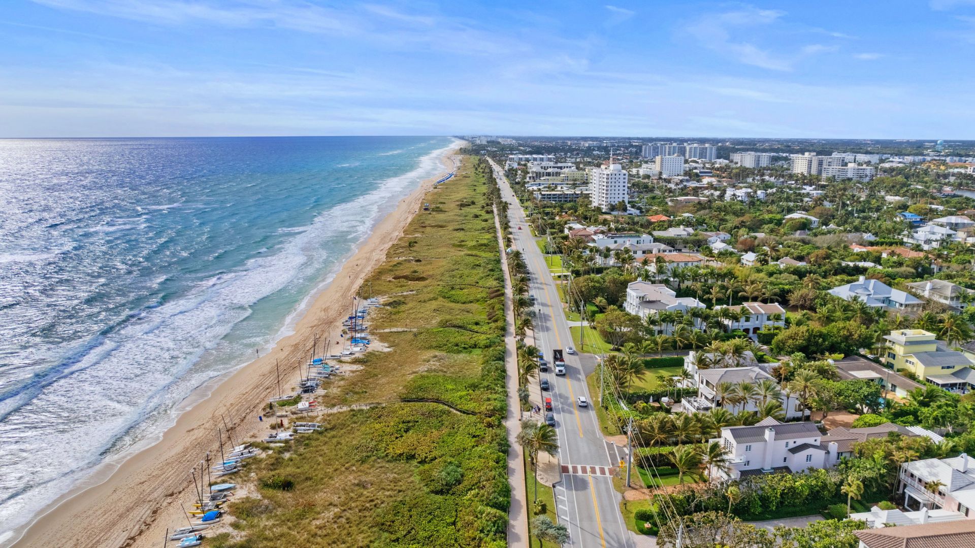 Aerial view of a beach with waves lapping at the shore, surrounded by colorful houses along the coastline.