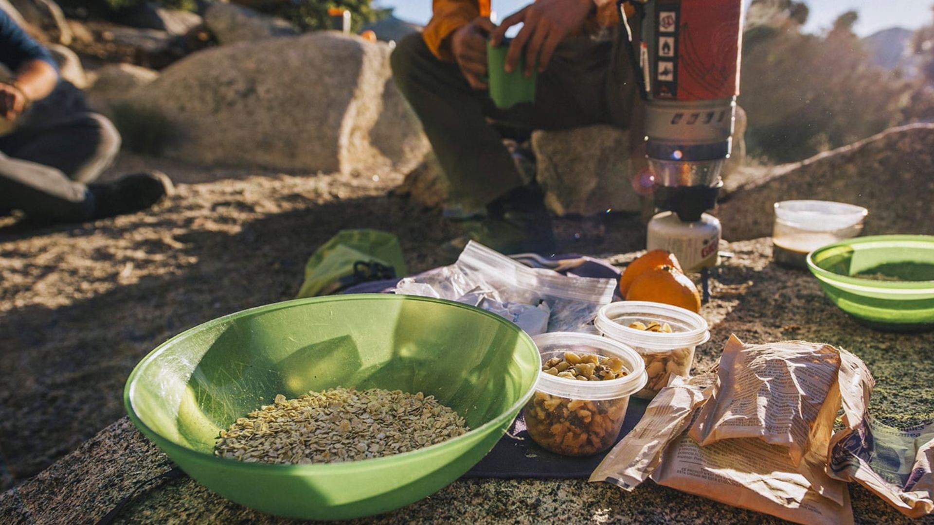 A person sitting on a rock, enjoying a bowl of food in a natural outdoor setting.