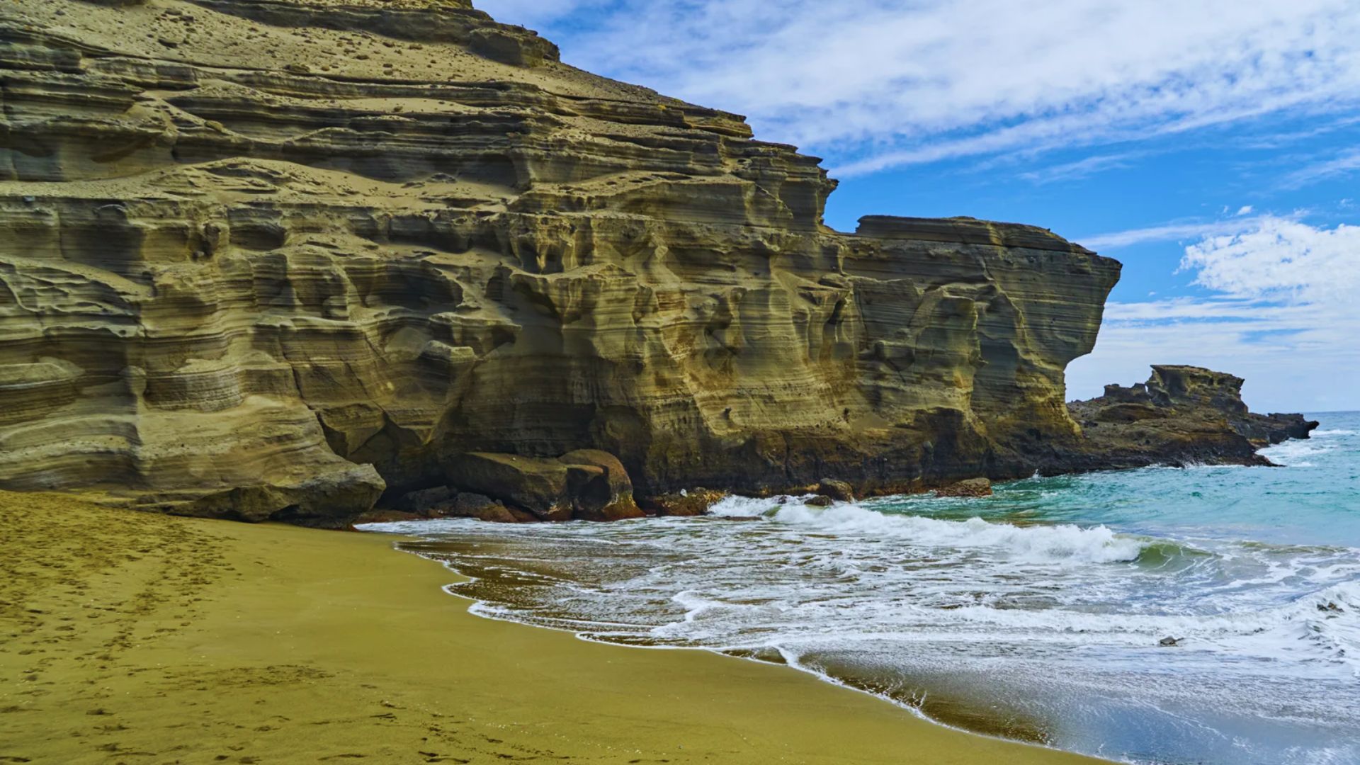 A scenic beach featuring a rocky cliff with waves gently crashing on the shore.