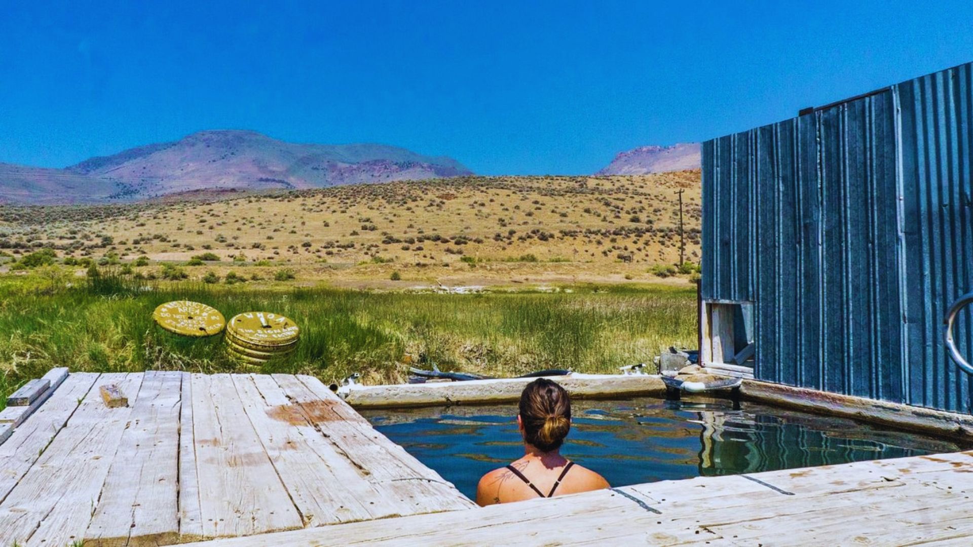 A woman relaxes in a hot tub with a scenic mountain backdrop.