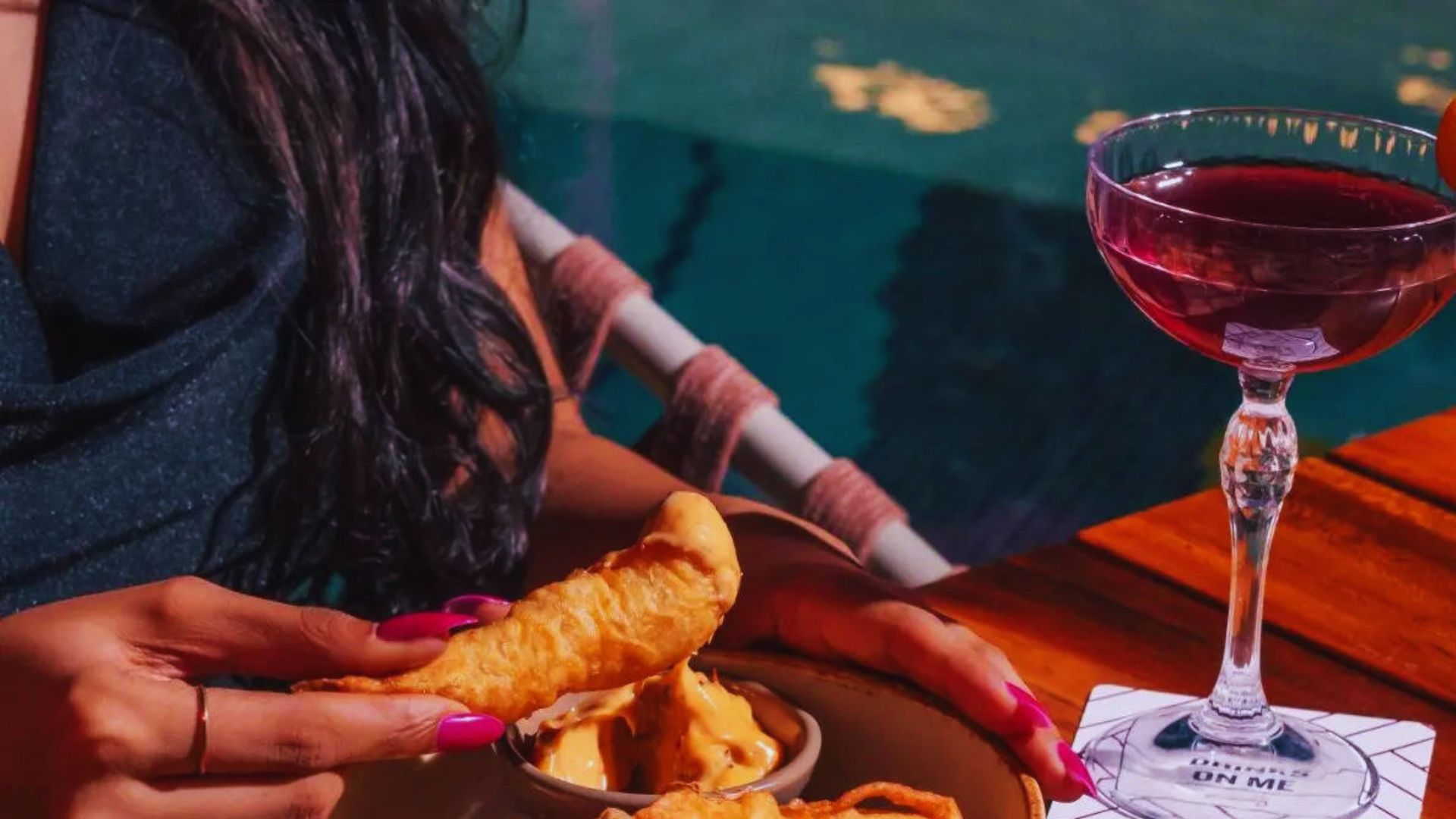 A woman enjoys a meal on a plate while sipping a glass of wine at a dining table.