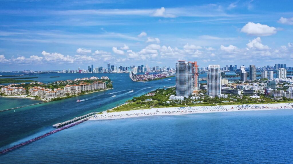 Miami vs Miami Beach: Which Is Best for Your Stay? Aerial view of Miami Beach: vibrant turquoise ocean, white sandy beaches, high-rise buildings, and a clear blue sky. A lively, tropical vibe.