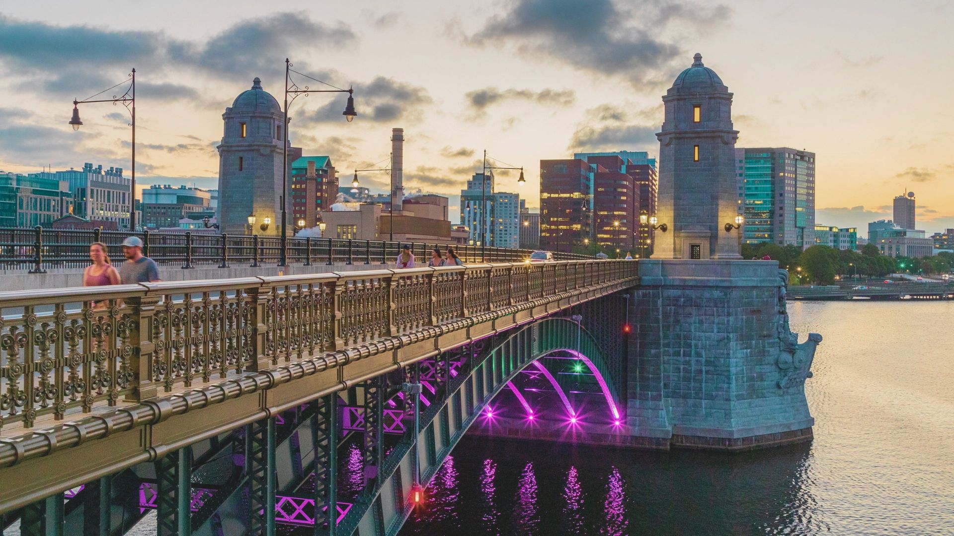 A bridge illuminated by purple light spans over calm water, creating a serene and enchanting nighttime scene.