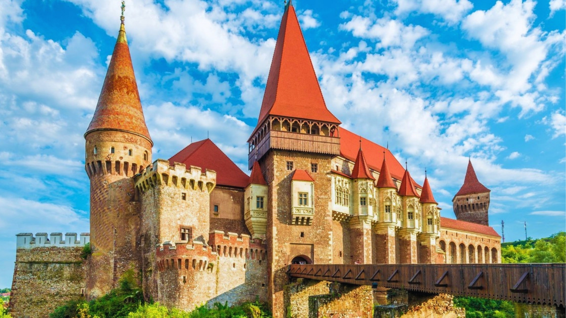 Medieval castle with red-roofed towers and stone walls set against a vibrant blue sky with clouds, conveying grandeur and historical significance.