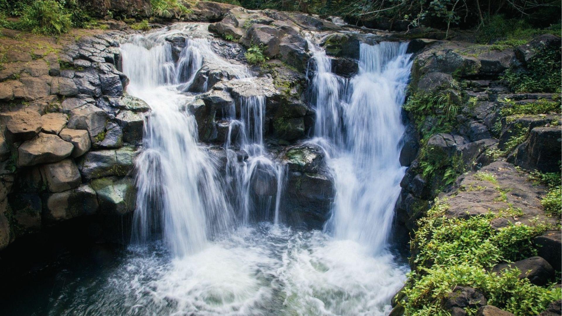 Ho'opi'i Falls Trail tumbled over dark lava rock into a pool on Ho'opi'i Falls Trail in Kauai.