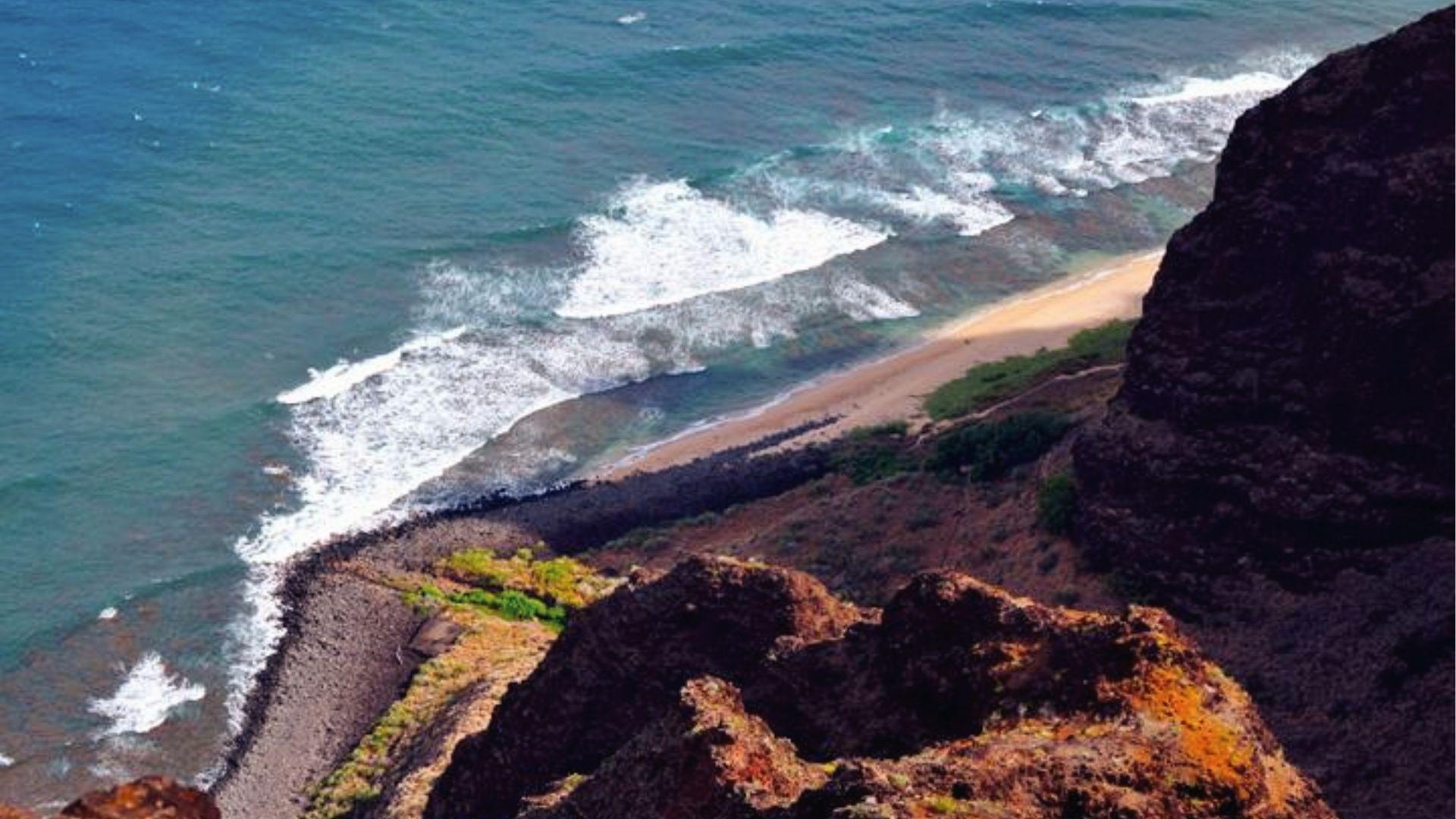 Awa'awapuhi Trail cliffside overlooks turquoise waves and secluded beach on Napali Coast.