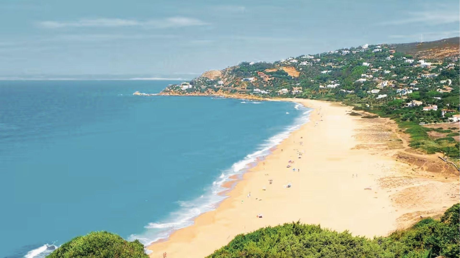 Costa de la Luz, Spain, golden sand curves along a quiet bay, hillside villas and green headlands meet the open sea.