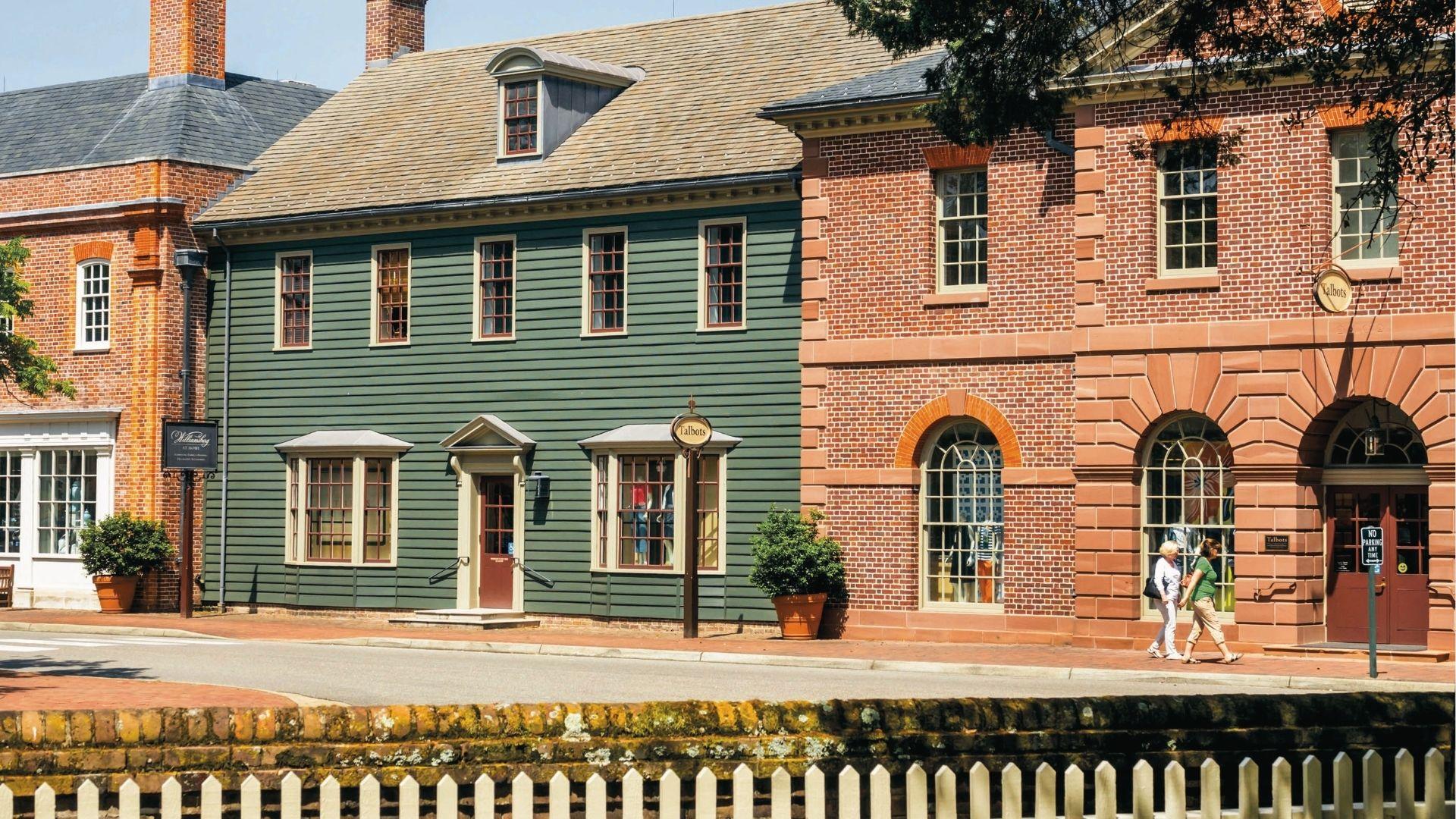 Colonial brick and clapboard shops line a sunny street in Williamsburg, Virginia on a spring day.