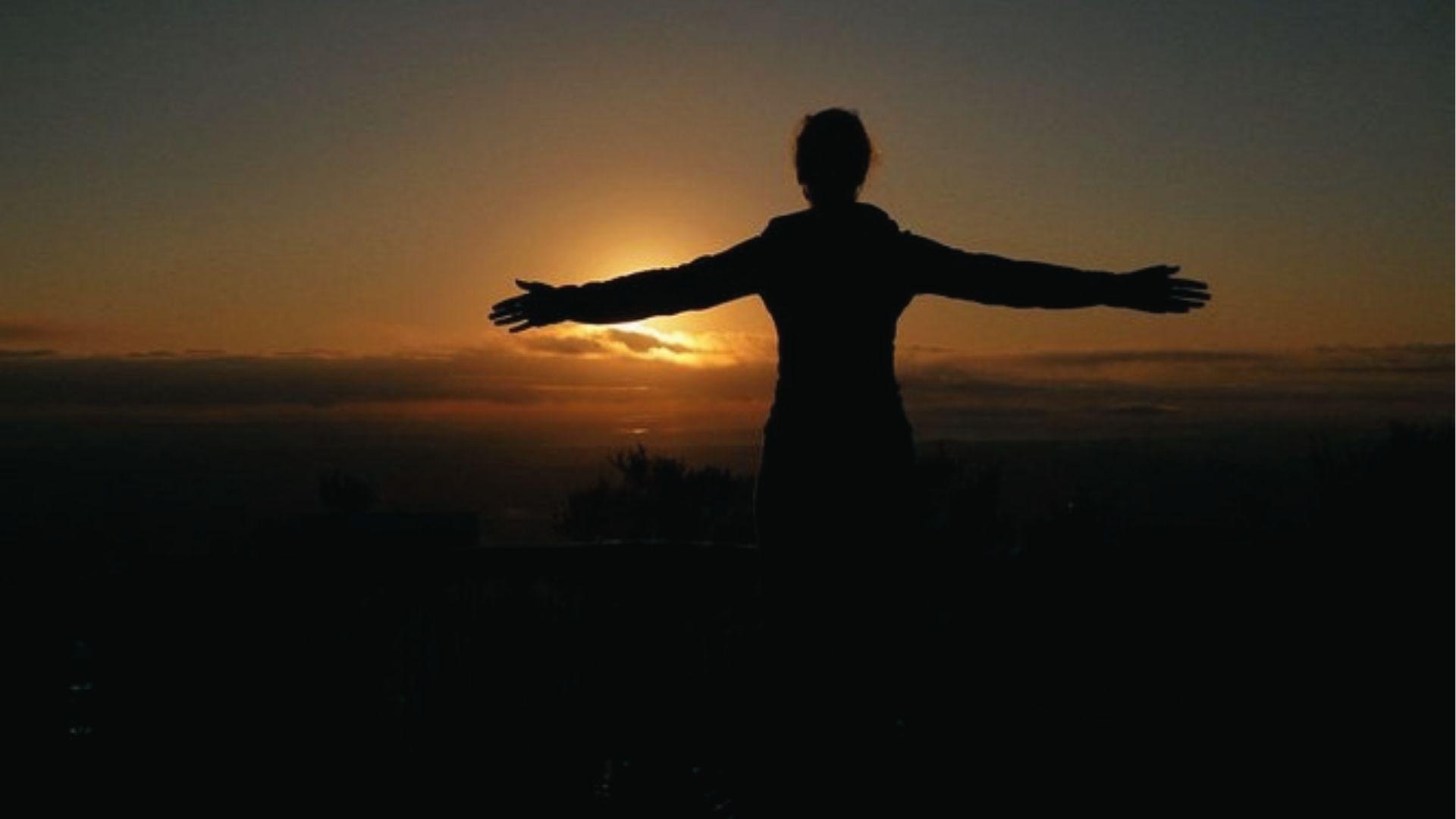 Watch a golden sunset with arms wide from a hilltop, enjoy peaceful views and quiet reflection.