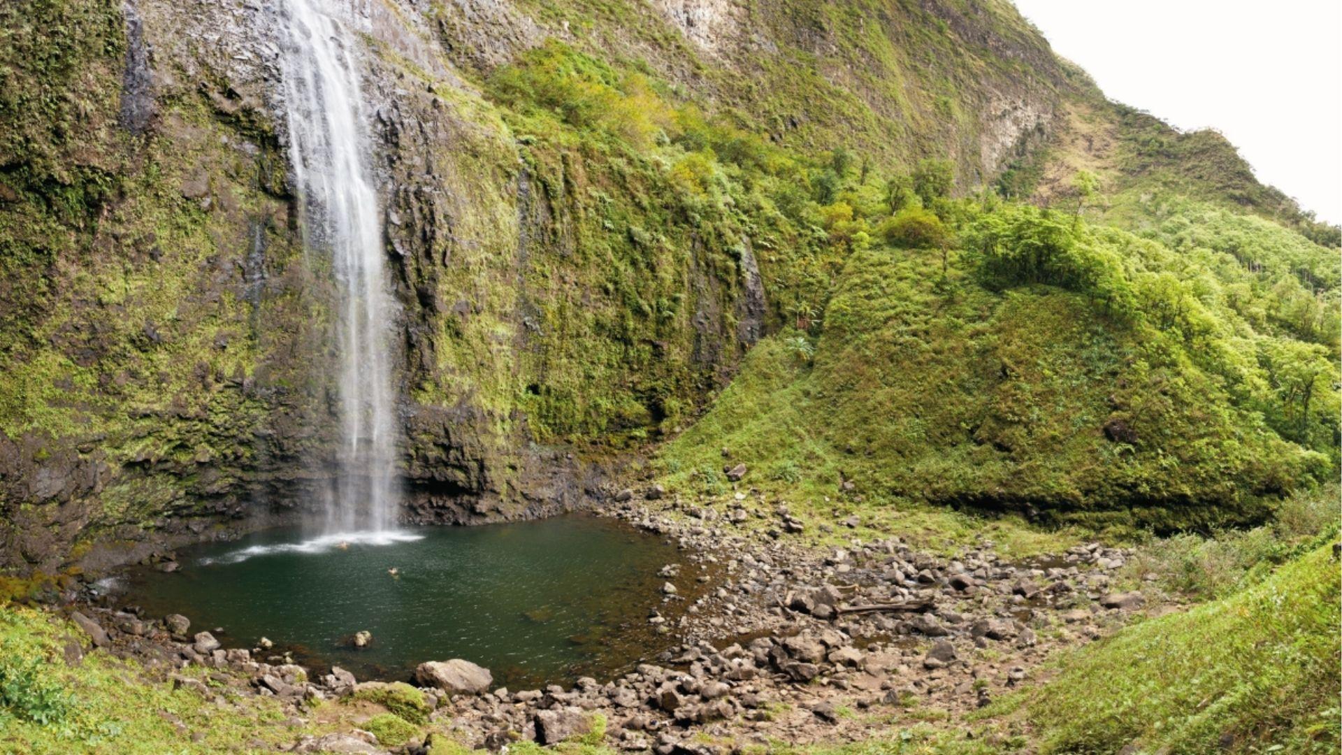 Towering Hanakapiai Falls plunges into an emerald pool surrounded by lush green valley walls.