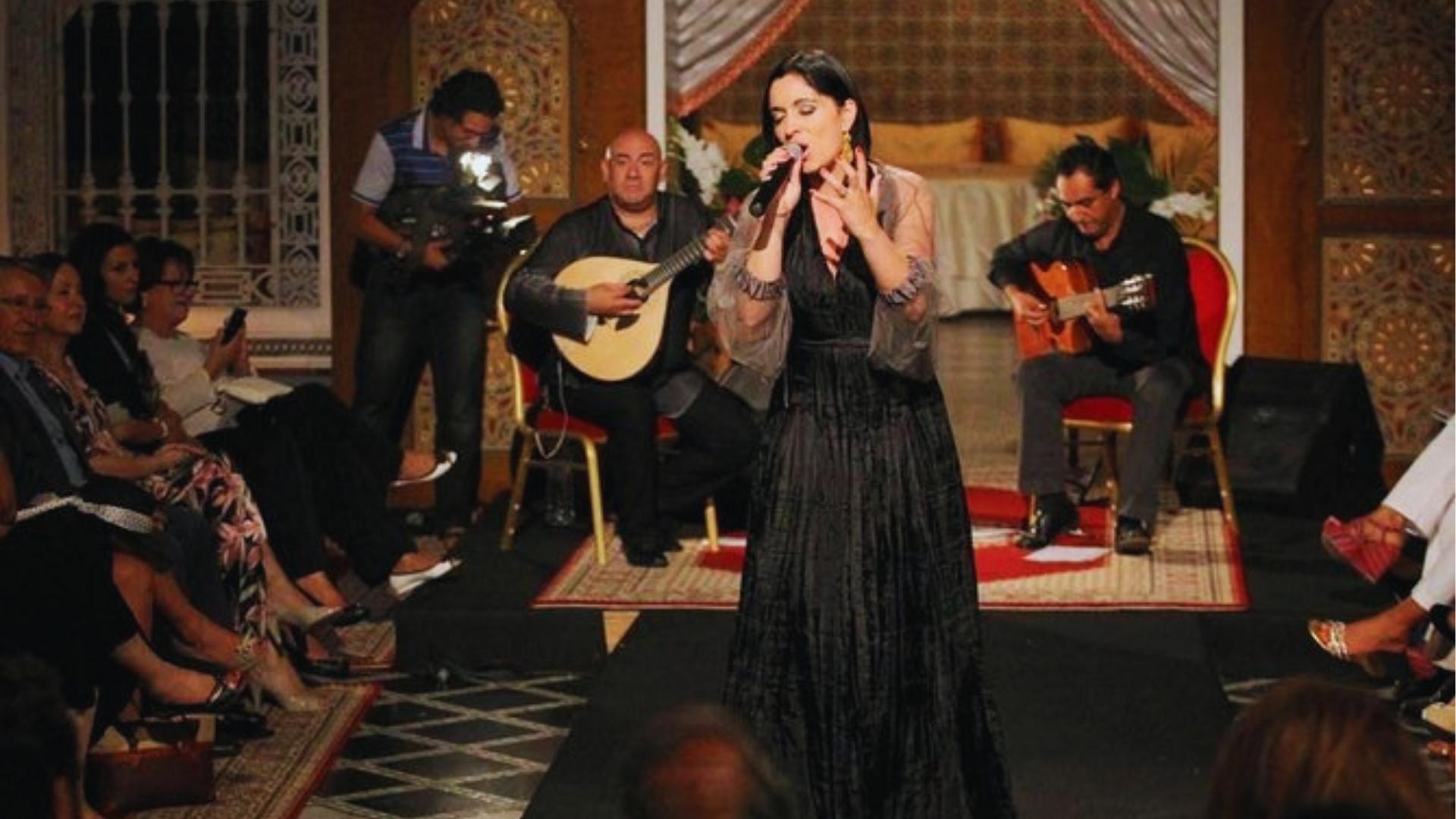 Fado singer in black dress performs with Portuguese guitarists for seated audience in intimate Lisbon venue with tiled walls.
