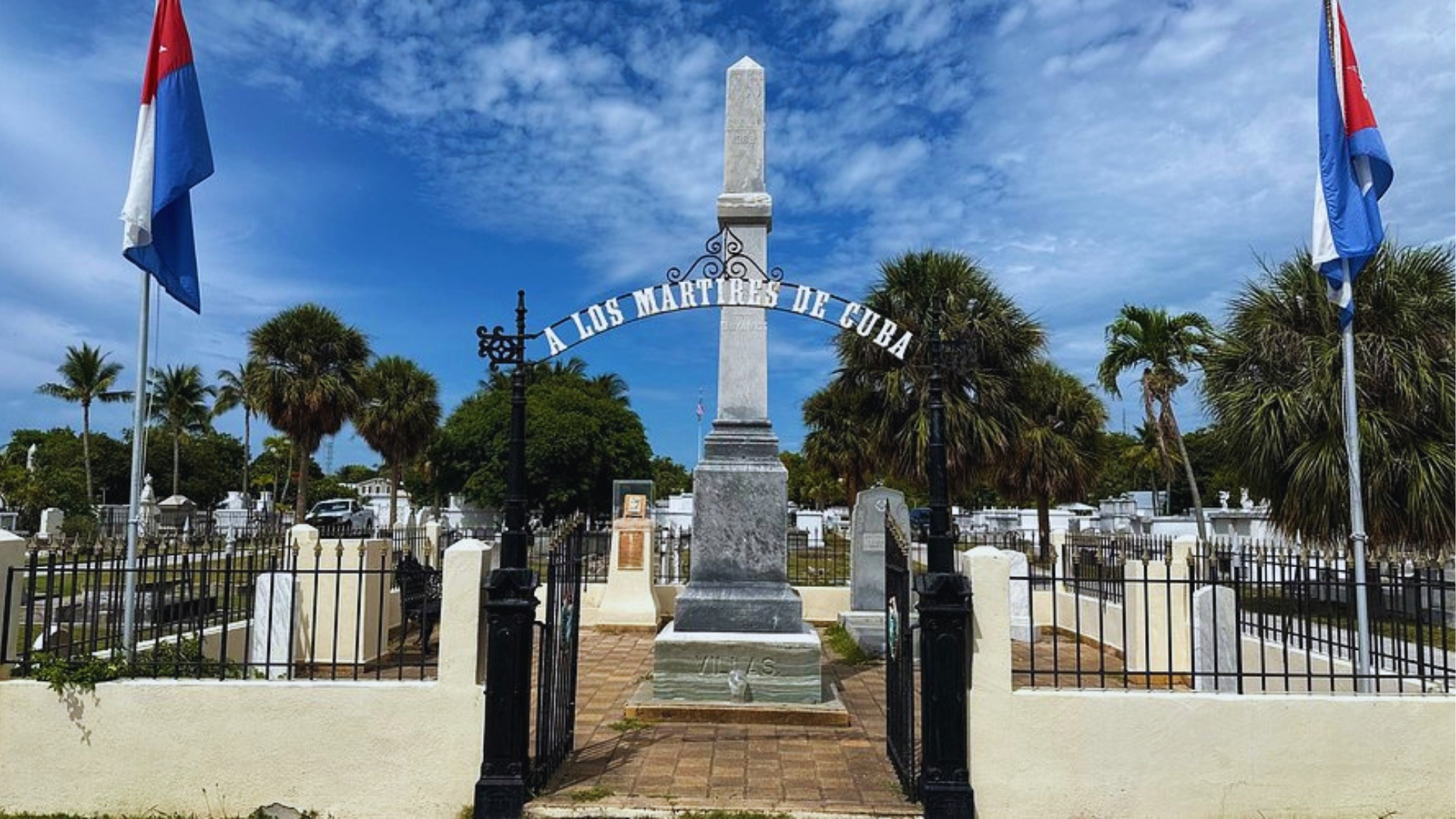 Historic A Los Martires de Cuba monument with arch, flags, and obelisk at Key West Cemetery under blue sky