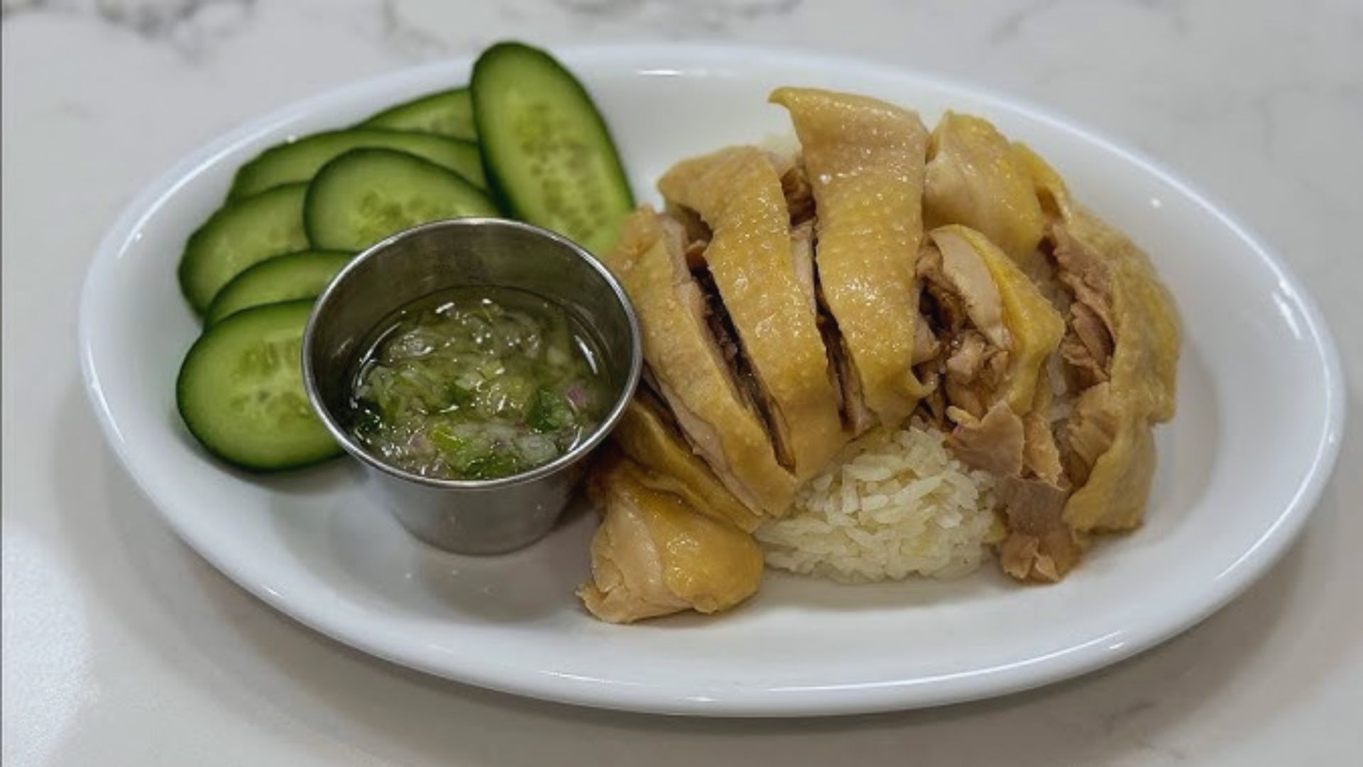 A plate featuring rice, sliced cucumbers, and grilled chicken arranged neatly.