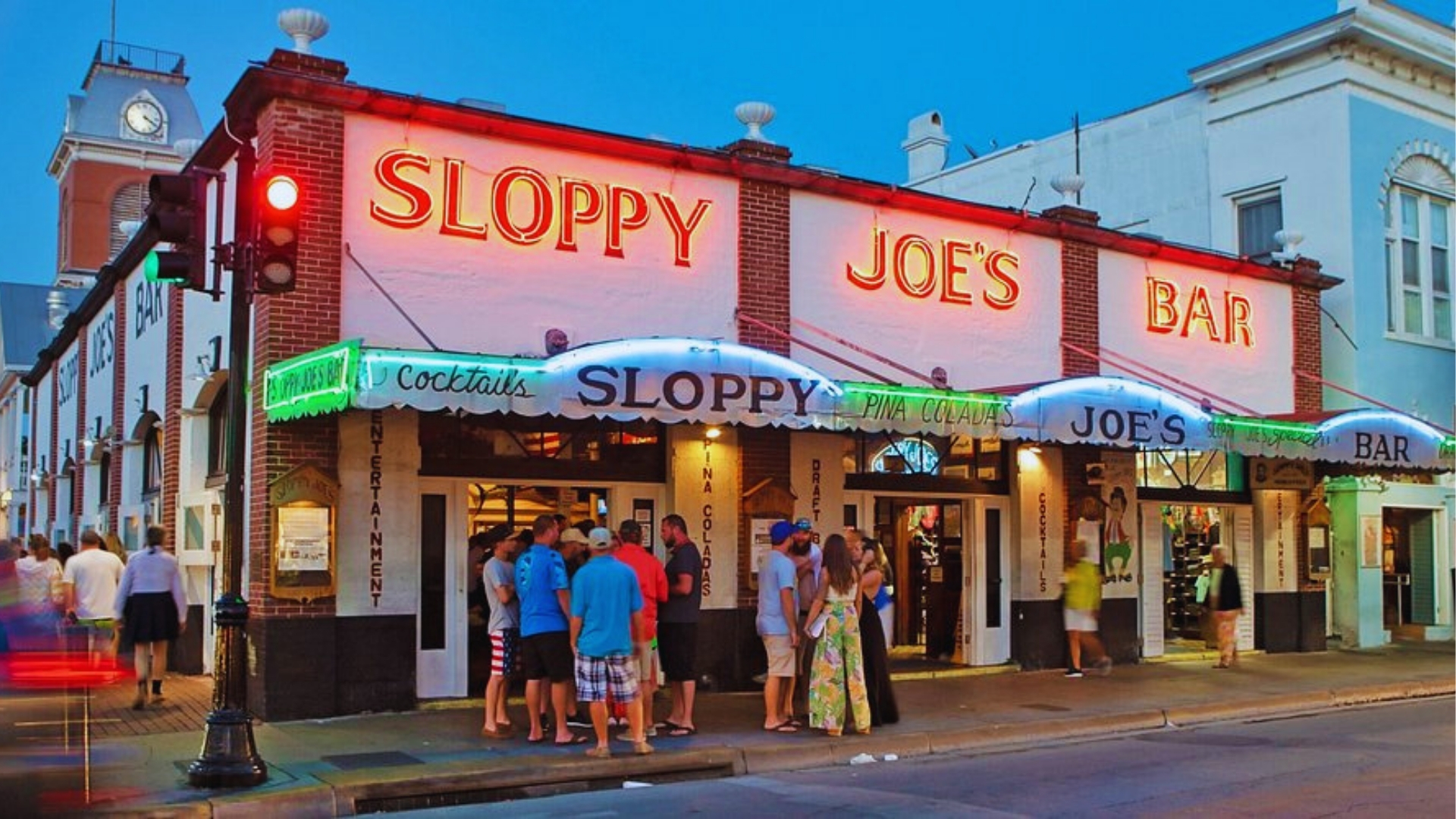 Sloppy Joe's Bar exterior at dusk with bright neon signs while crowds gather outside the iconic Key West landmark