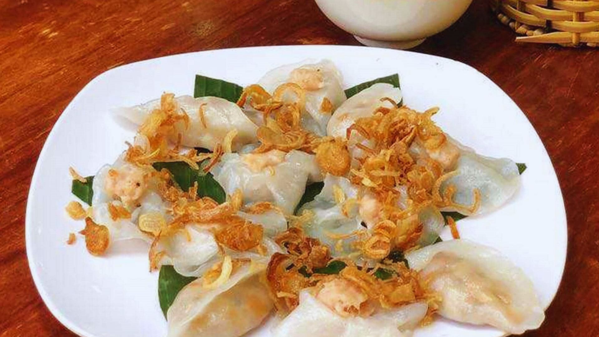 A plate of dumplings served with sauce alongside a steaming cup of tea.