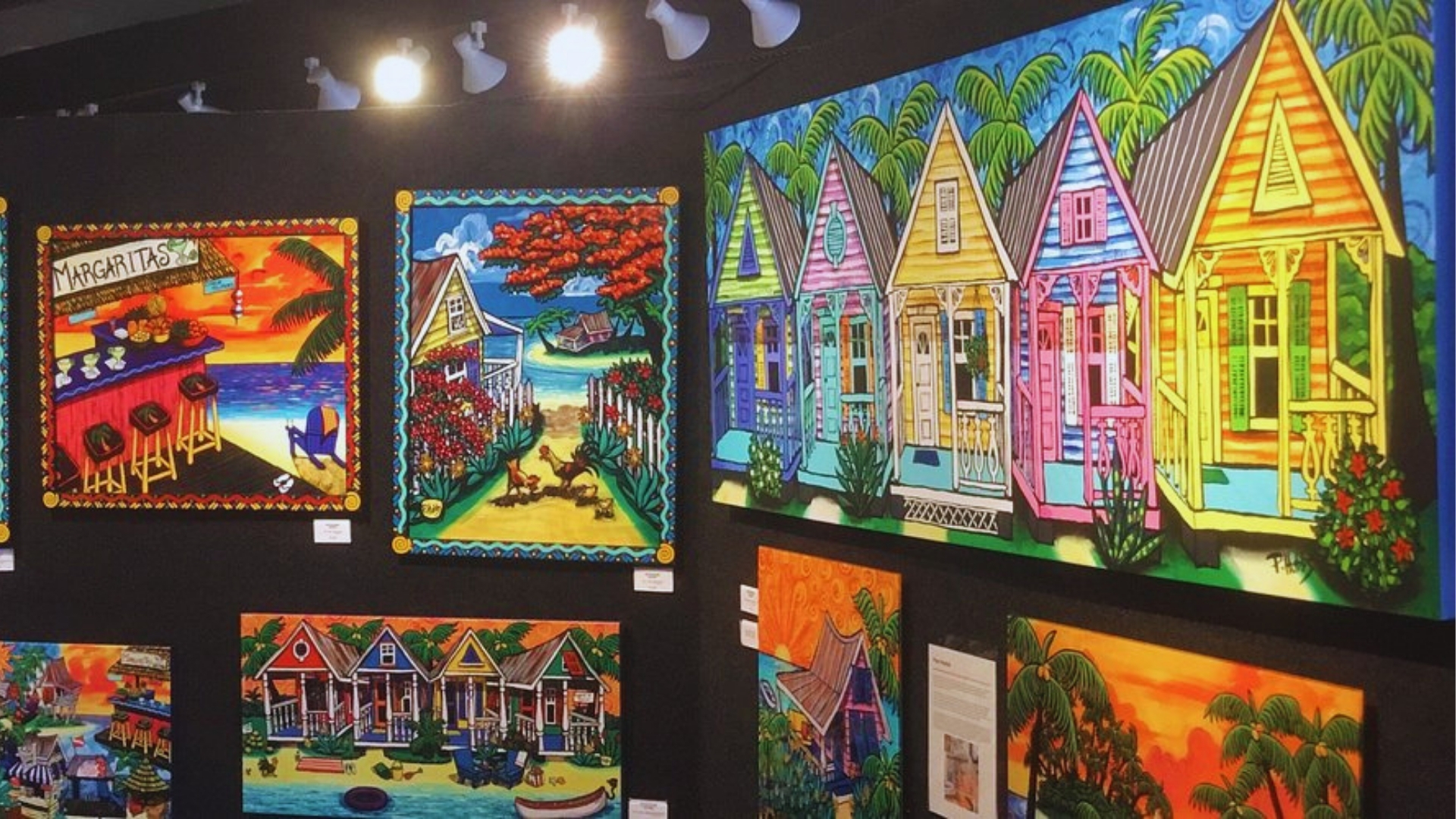 Colorful Key West folk art gallery wall featuring vibrant cottage paintings, palm trees, sunsets, and tropical beach scenes.