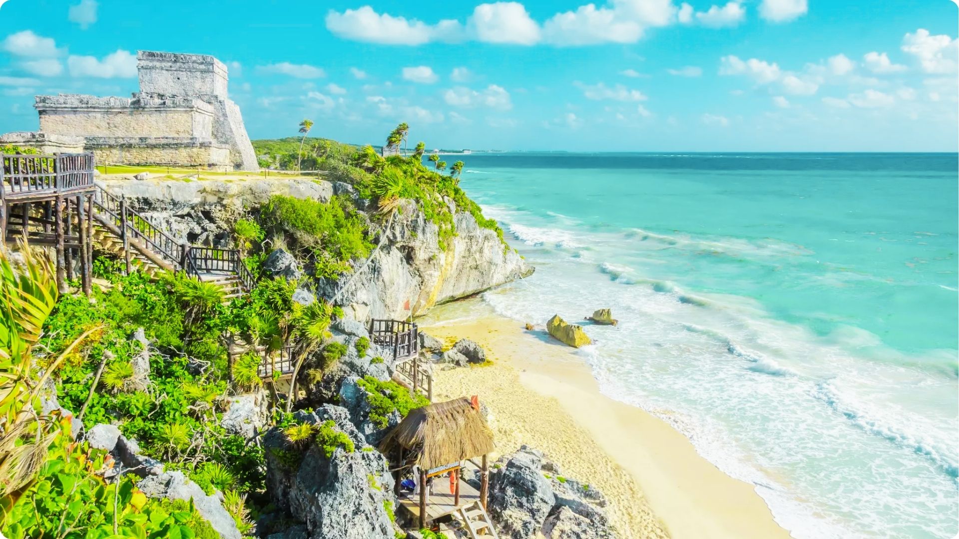 Ancient Mayan ruins overlook turquoise Caribbean waters and white sand at Tulum Beach.