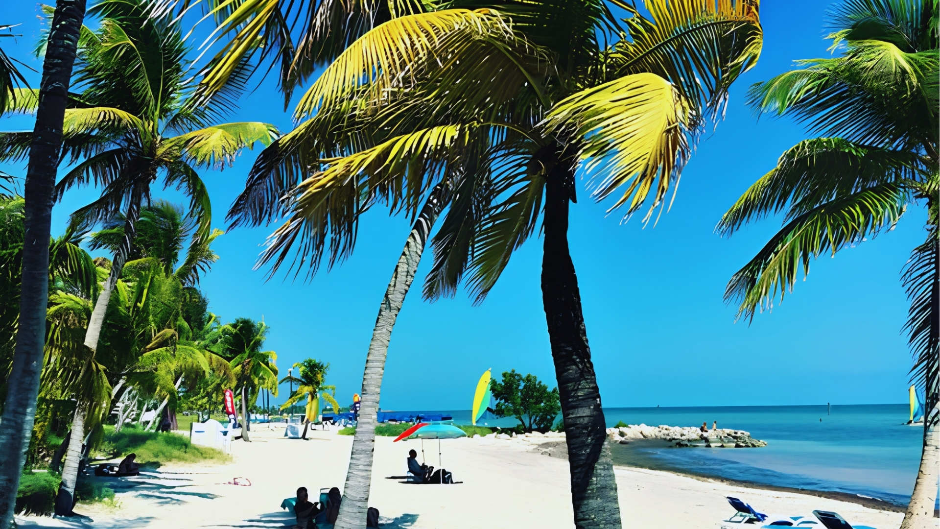 Smathers Beach in Key West with white sand, palm trees, colorful umbrella, and turquoise water under sunny sky.