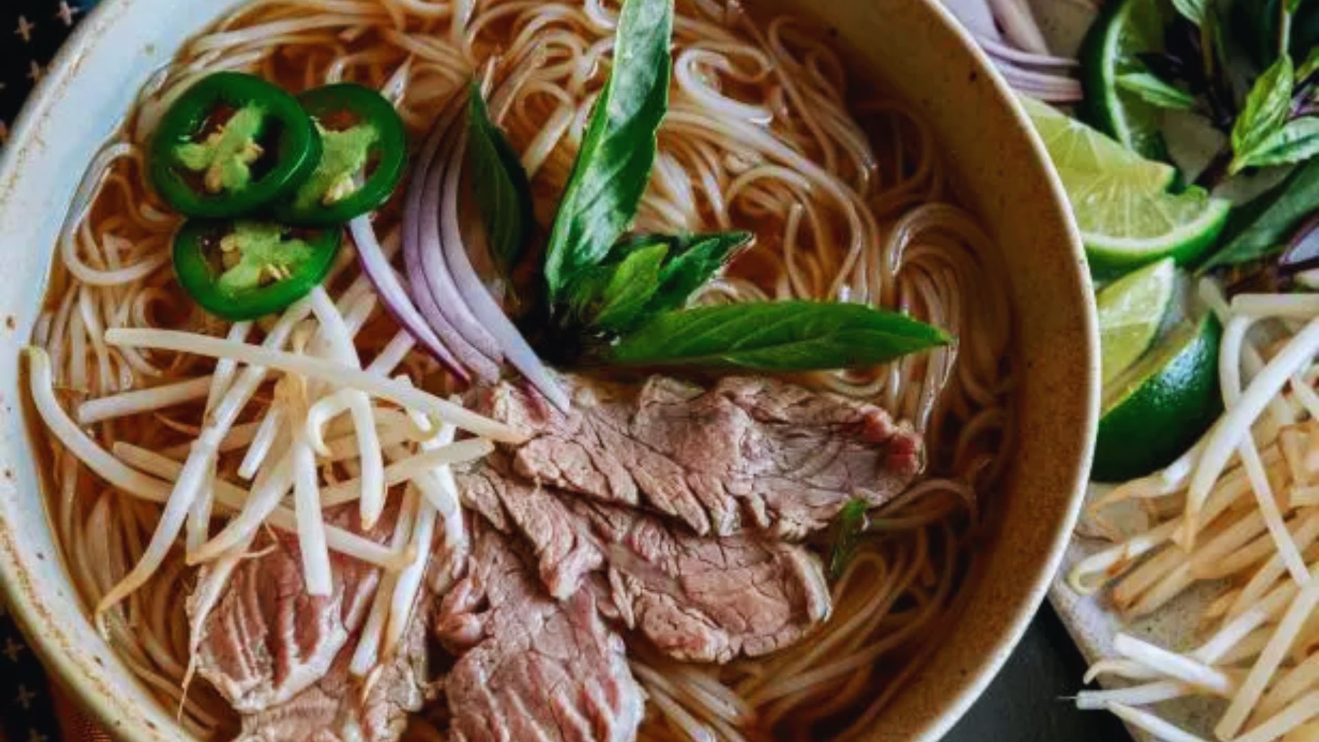 A bowl of beef pho filled with noodles, fresh vegetables, and aromatic broth, garnished with herbs