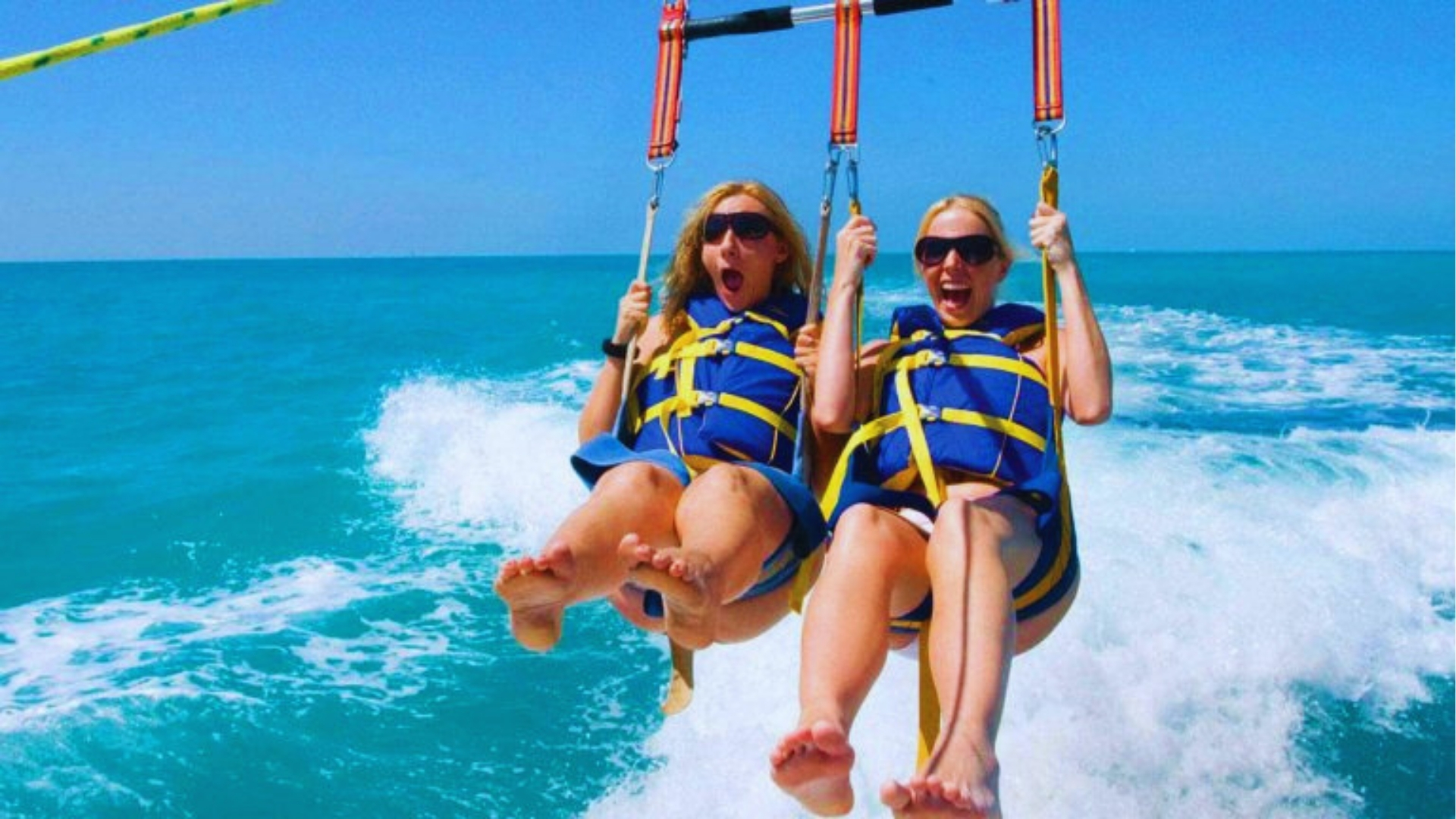 Two women in life jackets parasailing over turquoise ocean waters while screaming with excitement on Key West adventure.
