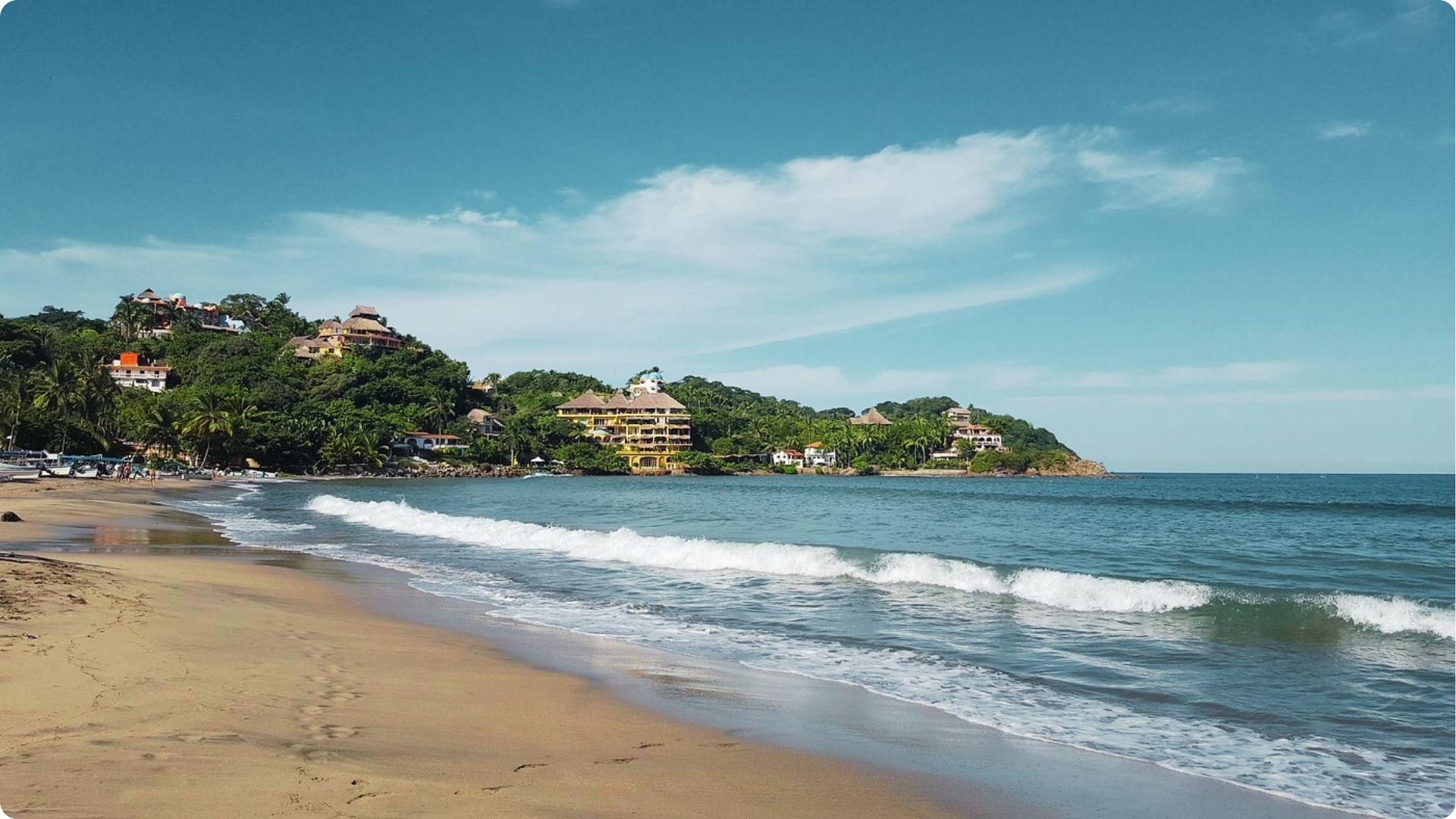 Gentle waves roll onto a golden beach backed by lush hills and hillside hotels.