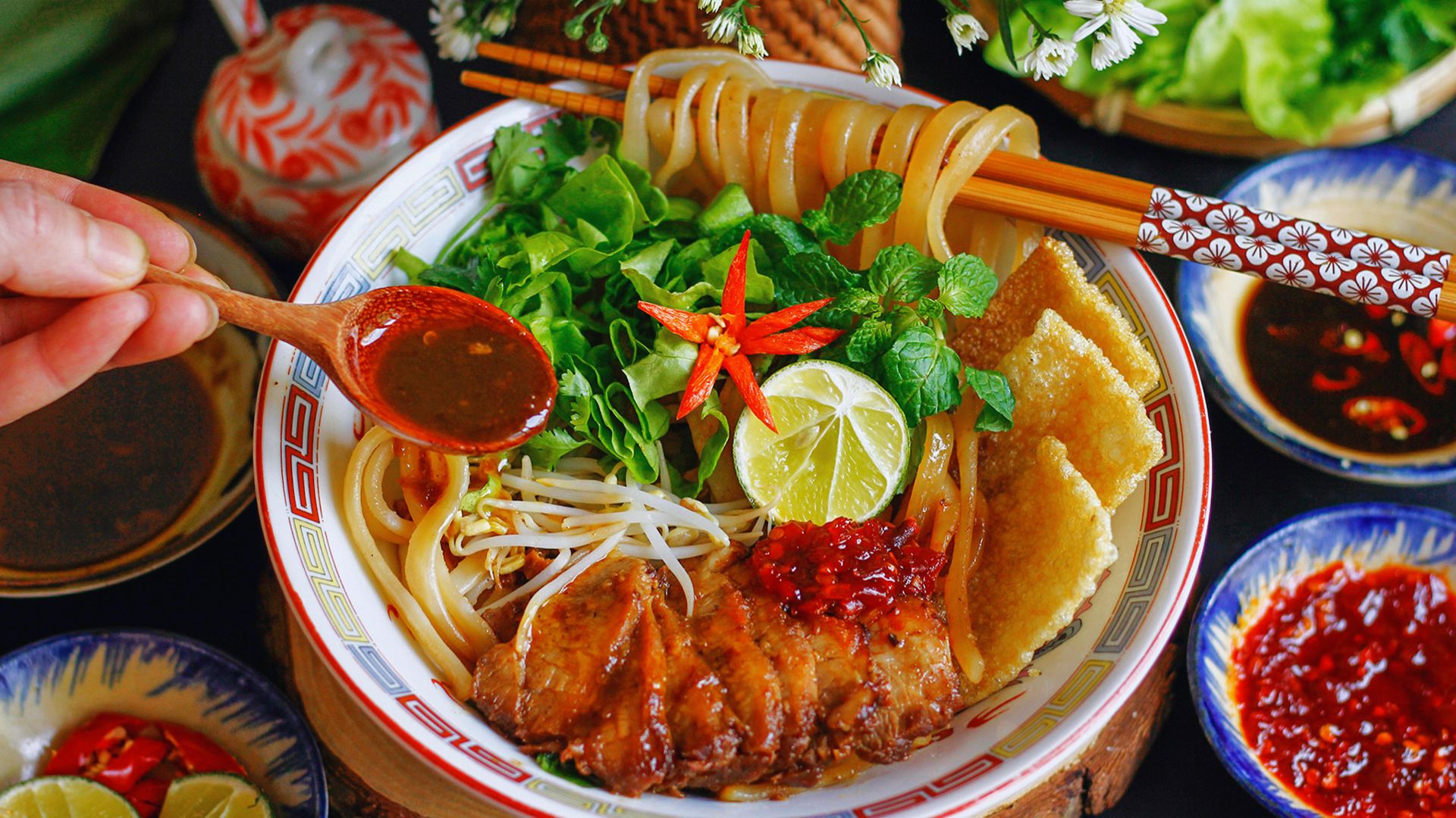 A bowl of noodles with chopsticks resting on the side, accompanied by a small dish of sauce.