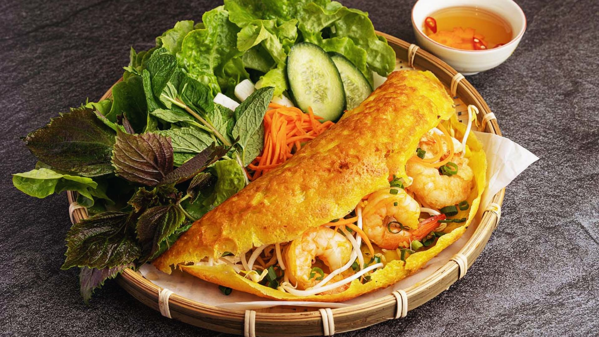 A bamboo basket containing a sandwich and a fresh salad, arranged neatly for a picnic or meal setting.