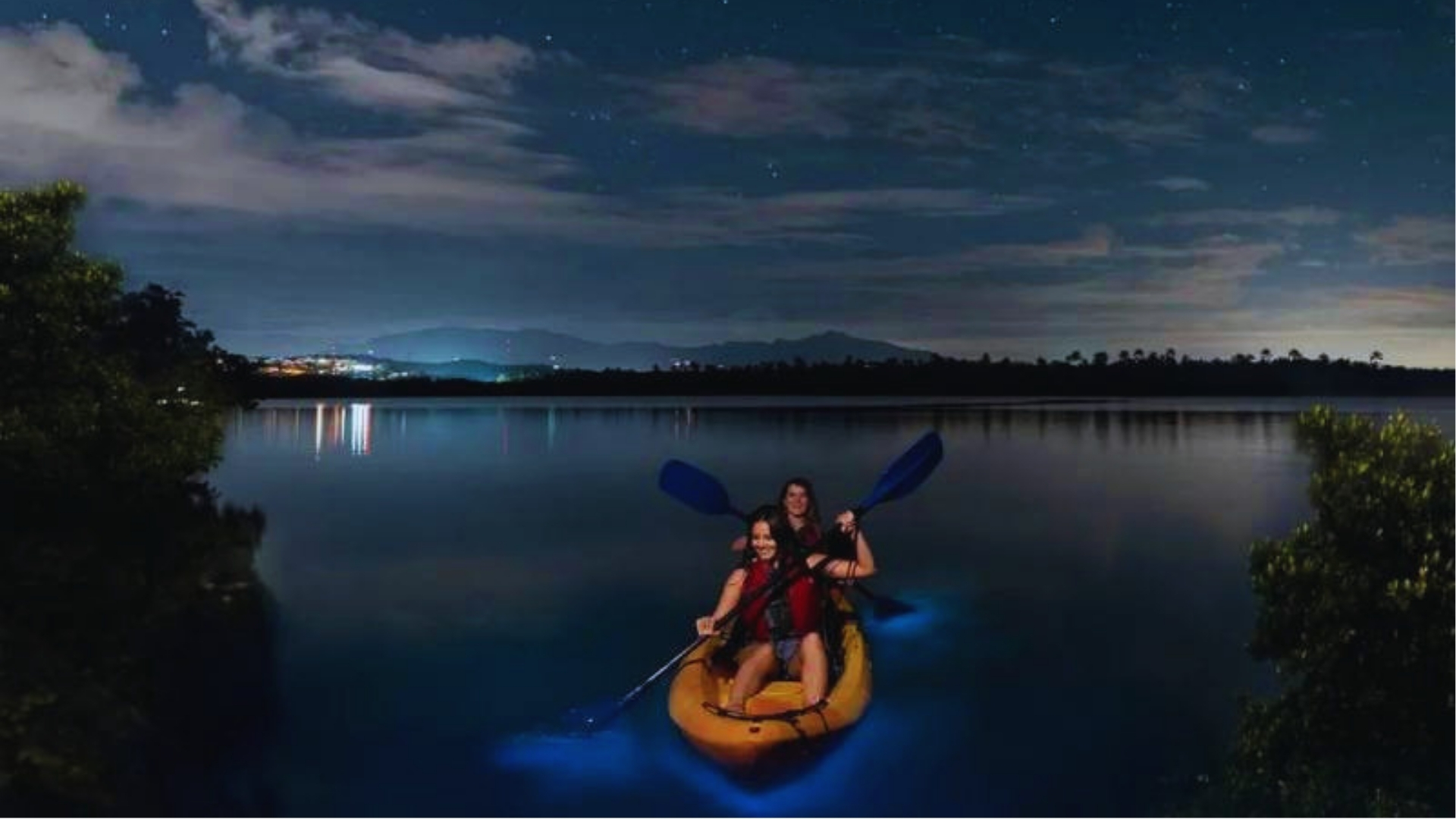 Girls kayaking at night through glowing bioluminescent water under starry sky during Key West eco tour.