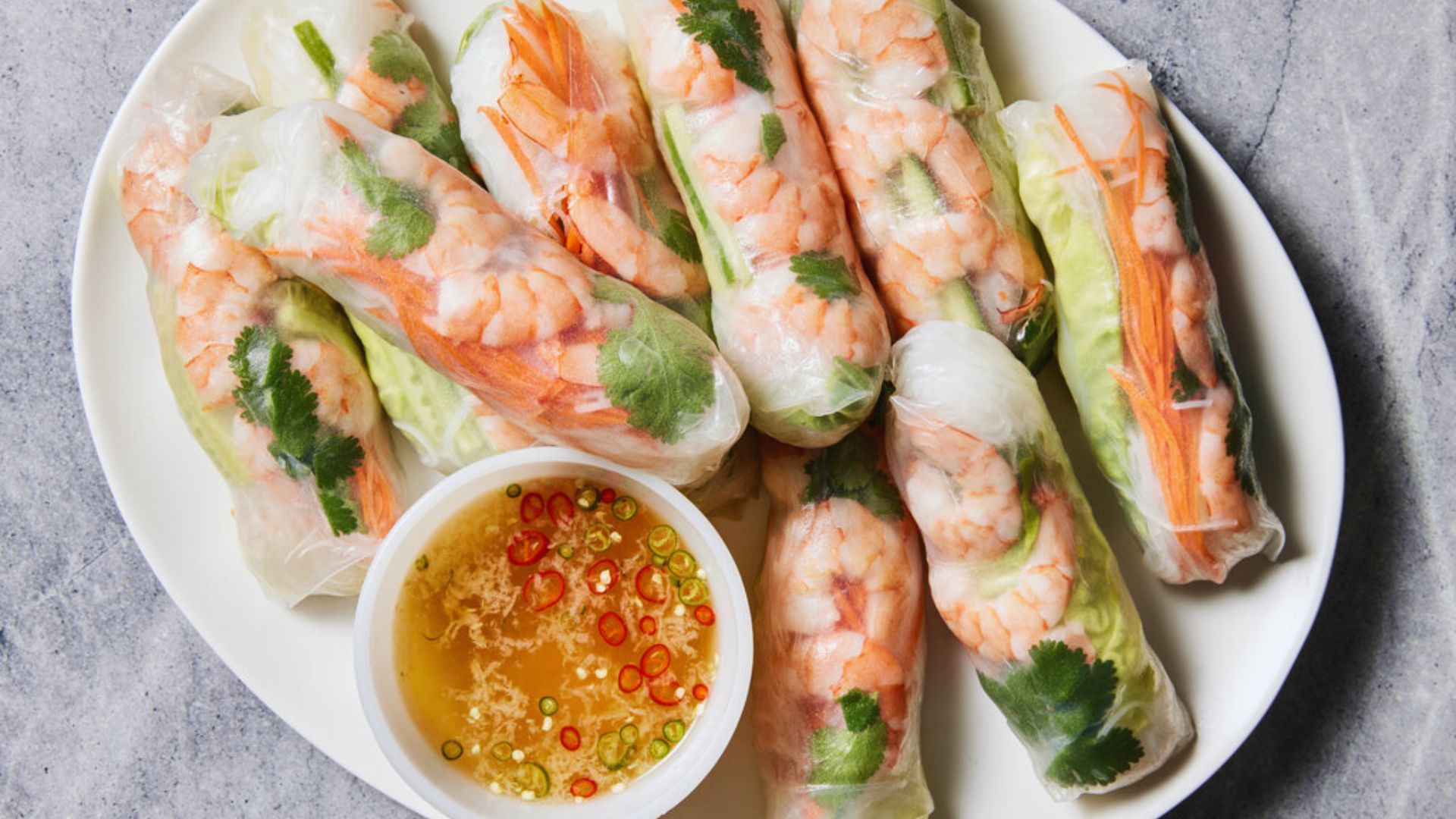 A plate of shrimp spring rolls served with a small bowl of dipping sauce on the side.