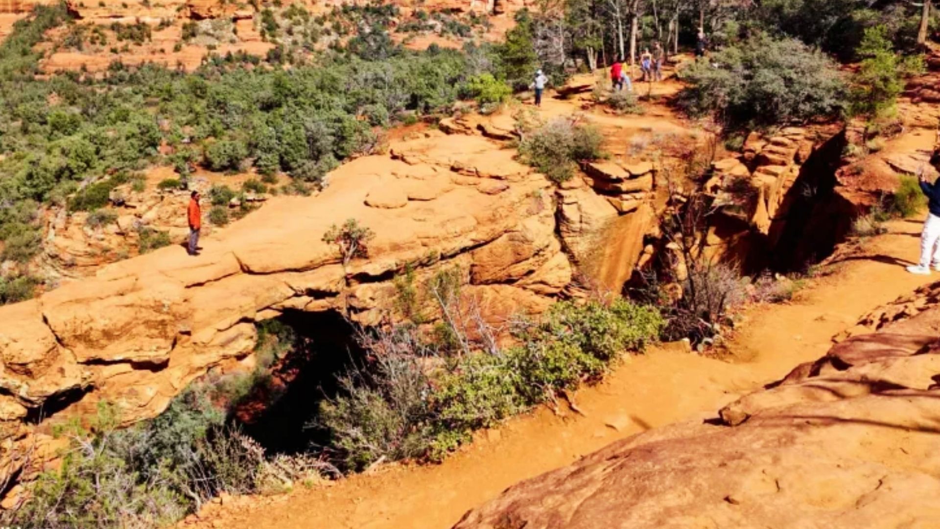 Tourists standing on Devils Bridge natural sandstone arch with Sedona red rock canyon views behind them