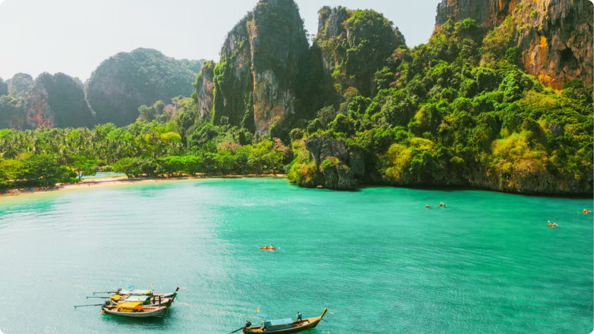 Traditional longtail boats float on turquoise water beneath towering limestone cliffs.
