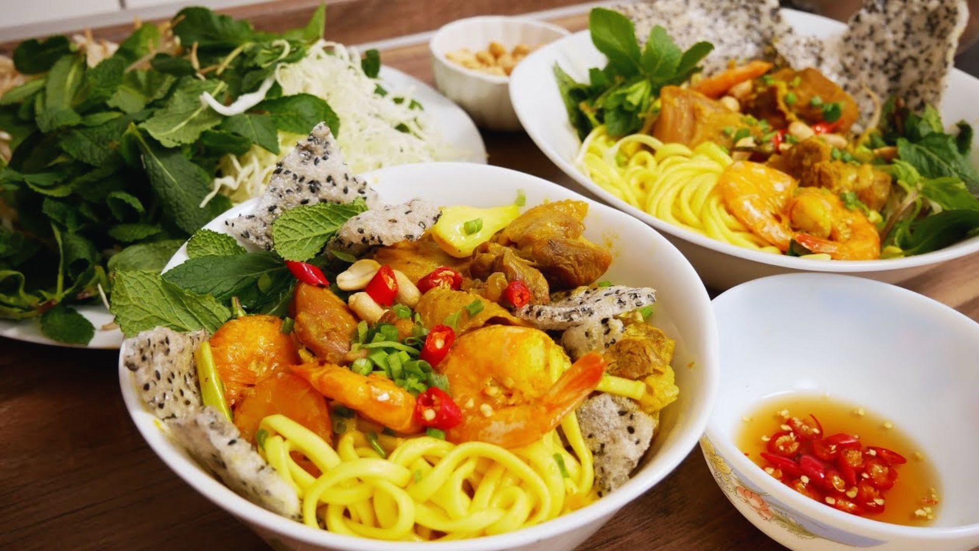 Two bowls of noodles topped with colorful vegetables and shrimp, arranged appetizingly on a wooden table.