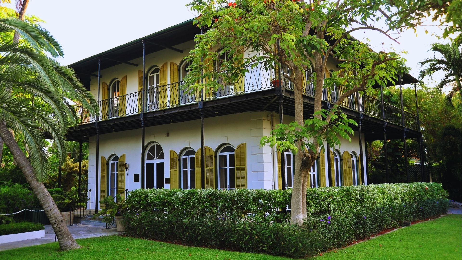 Ernest Hemingway Home and Museum exterior with yellow shutters, black balcony, and tropical gardens in Key West.