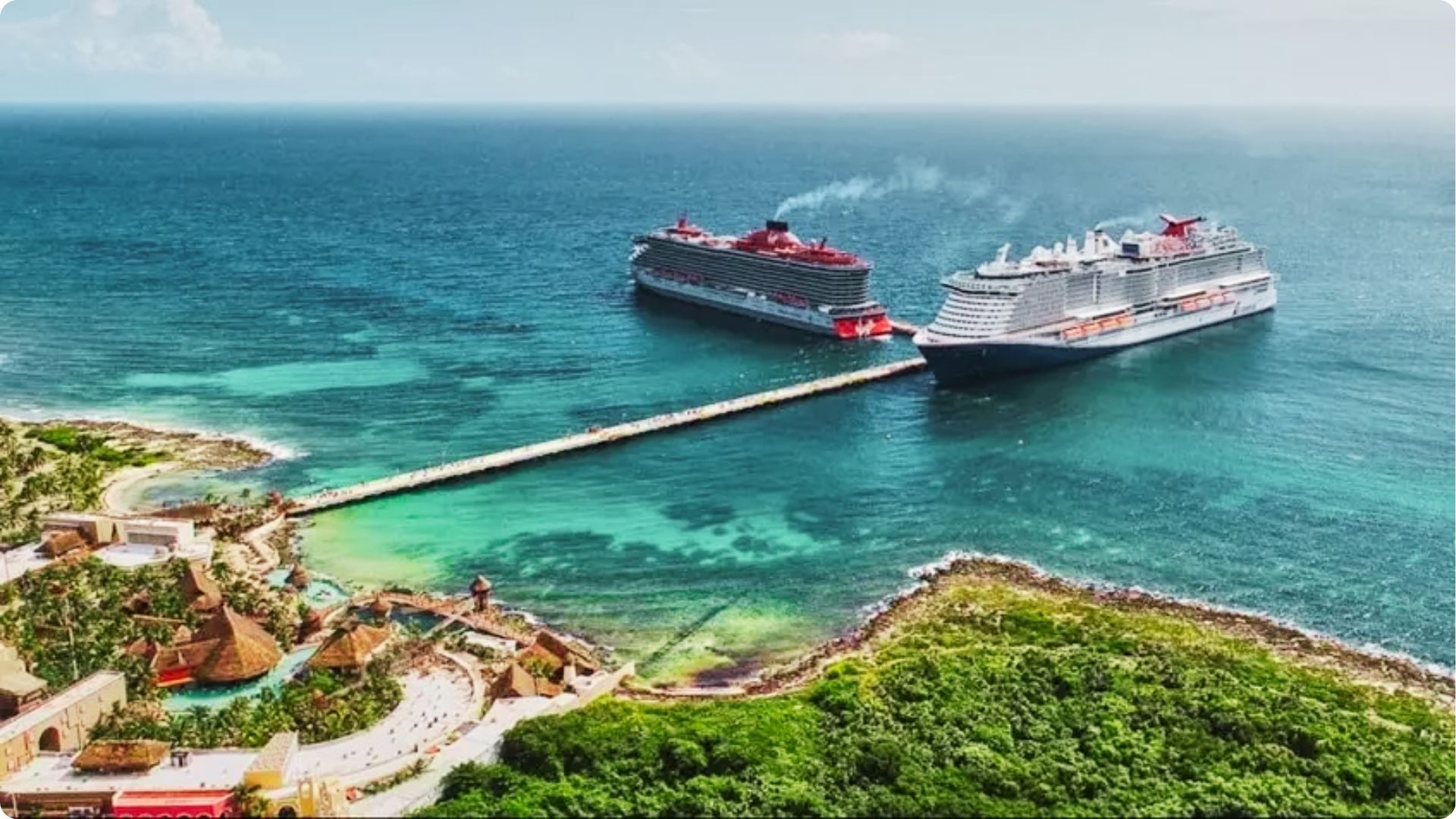 Two large cruise ships docked at a long pier extending into turquoise Caribbean waters