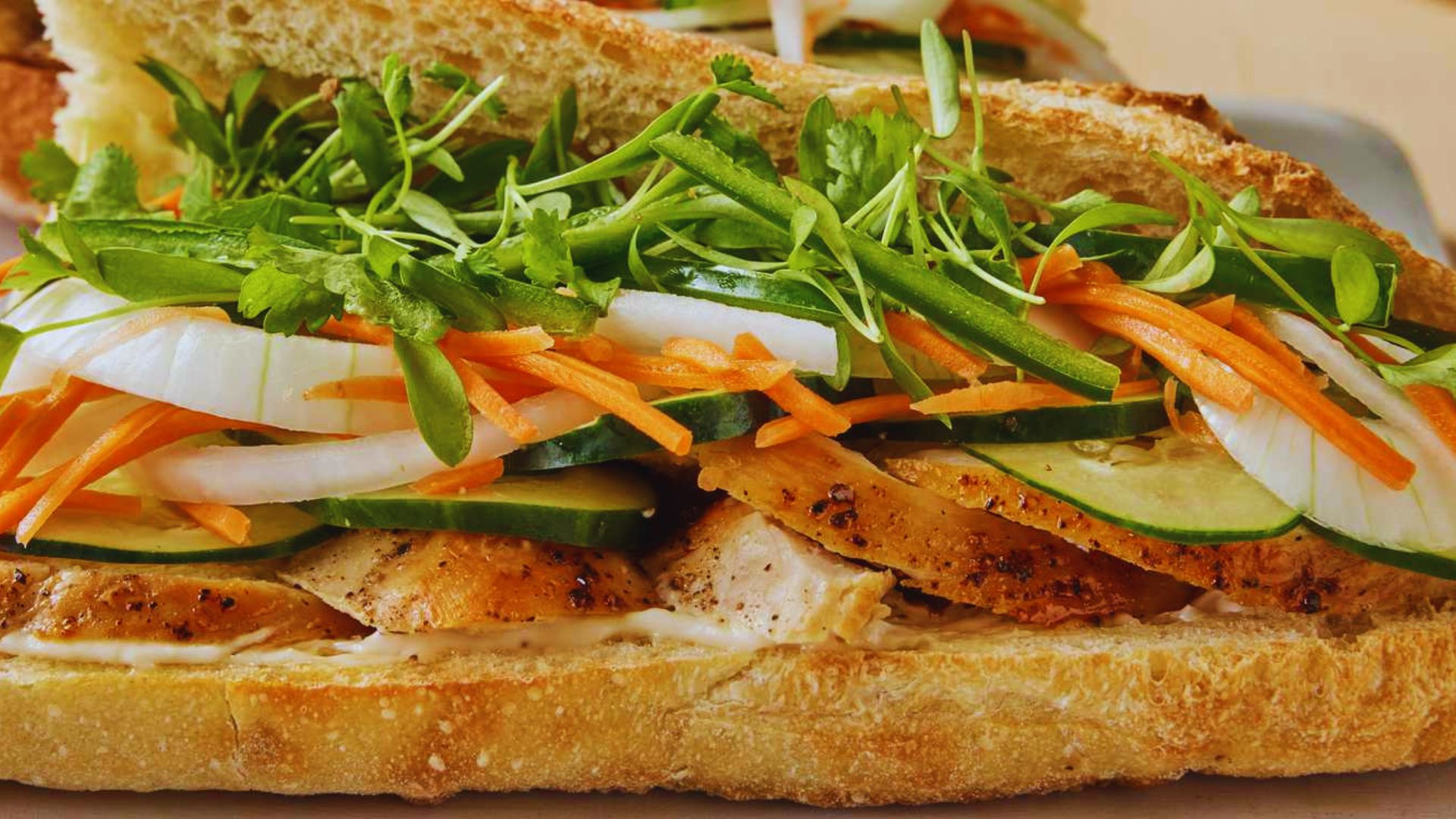 A sandwich filled with fresh vegetables and meat, served on a white plate.