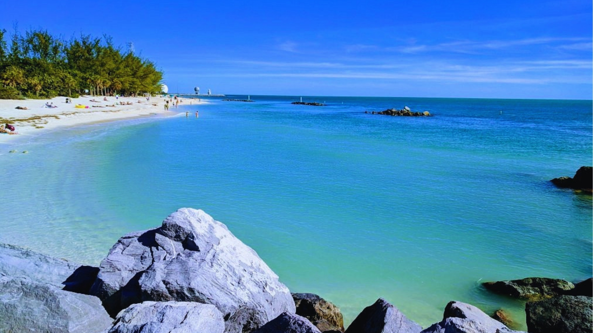 Turquoise shallows and rocky jetty at Fort Zachary Taylor Beach in Key West, with swimmers and white sand.