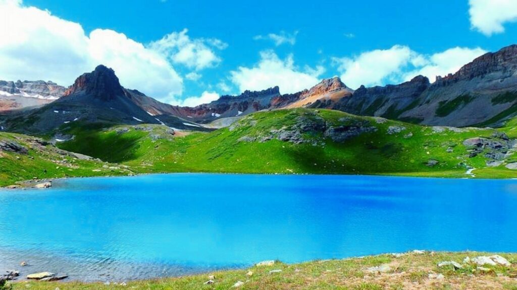 Ice Lake Colorado Trail Guide: Tips, Map & Reviews Vivid turquoise Ice Lake Colorado glows under blue sky, framed by green alpine slopes and jagged San Juan Mountains peaks.