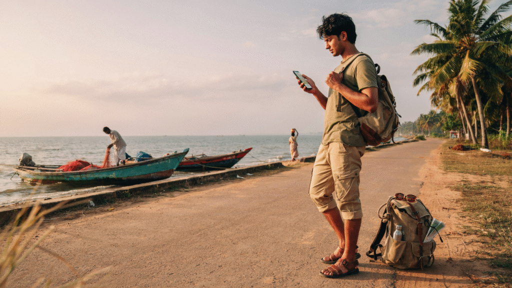 A man with a backpack stands on the road, looking at his phone, appearing focused and engaged with the device.