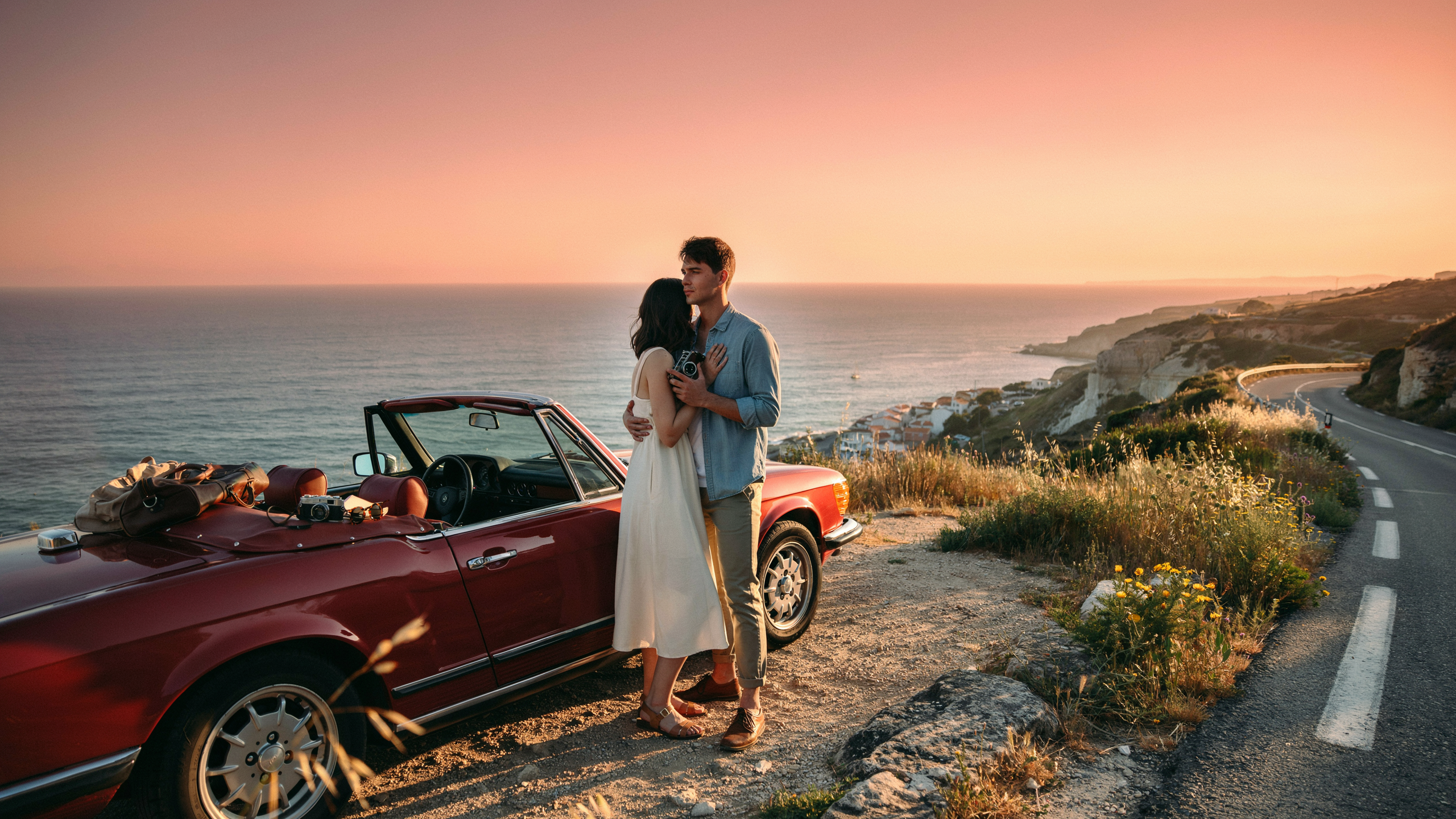 Couple kissing on a quiet road during a vibrant sunset, with warm colors illuminating the scene.