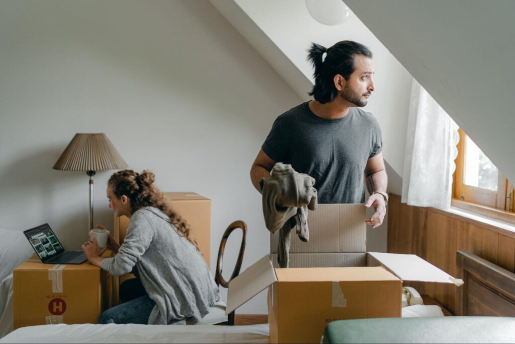 Why Relocating Can Feel Like Your Greatest Adventure Yet A man and woman are carrying boxes into a bedroom, preparing for a move or organizing their space.